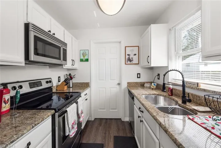 Kitchen featuring stainless steel appliances, white cabinets, dark wood-style flooring, and light stone counters