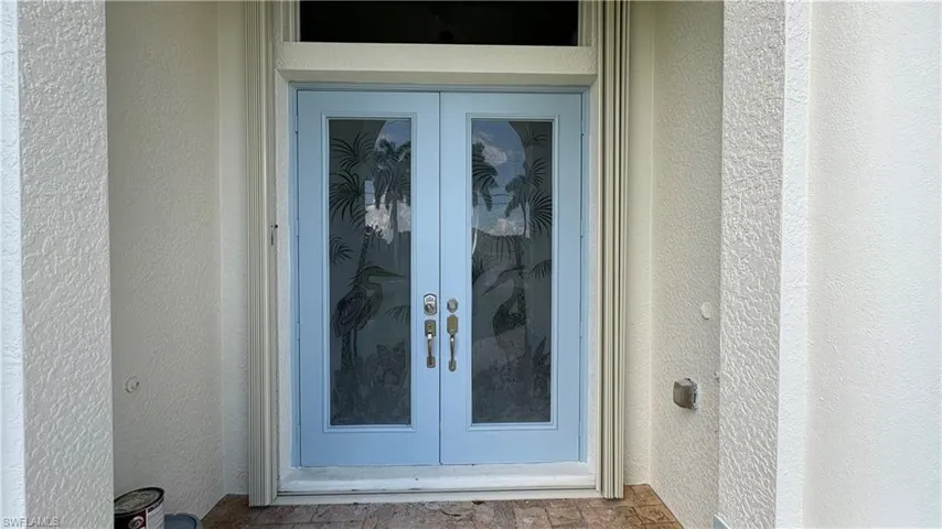 Double entry doors with decorative glass inserts featuring a heron and palm tree motif, light blue finish, and brass hardware