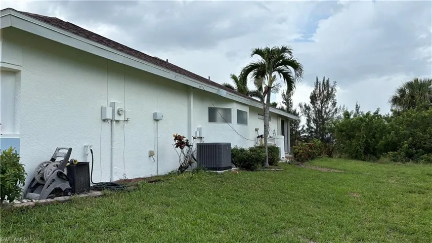 White stucco exterior with a brown shingle roof, featuring a mature palm tree and natural landscaping
