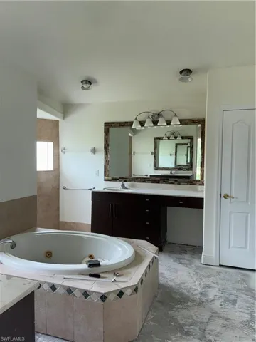 Spa-inspired master bath featuring a sunken soaking tub with tile surround, dual-sink vanity with black cabinetry and ample counter space, large framed mirror with integrated lighting, and recessed ceiling fixtures