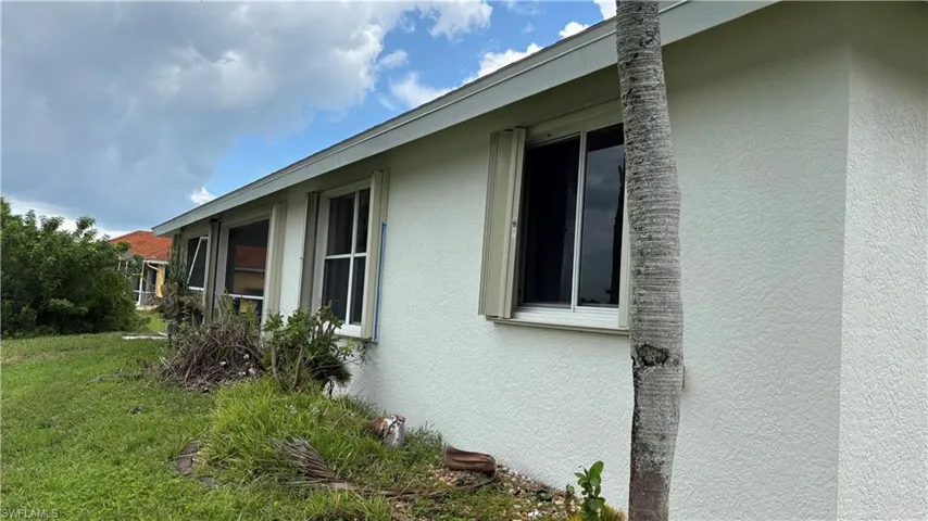 Exterior stucco walls featuring multiple windows with hurricane shutters and a mature palm tree