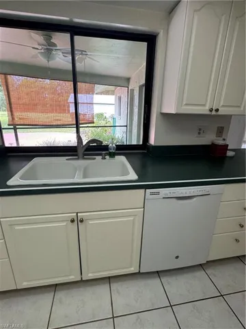Kitchen with dark countertops, white cabinetry, dishwashing machine, and light tile patterned floors