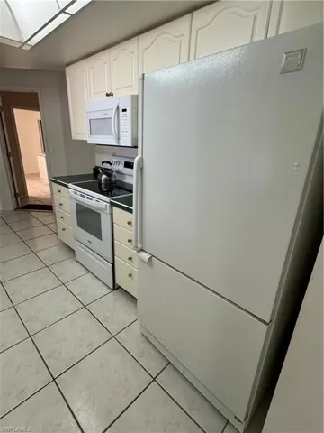 Kitchen featuring refrigerator, white stove, light tile patterned flooring, and white cabinets