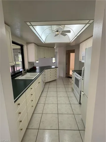 Kitchen with light tile patterned floors, white cabinetry, refrigerator, range, and a ceiling fan
