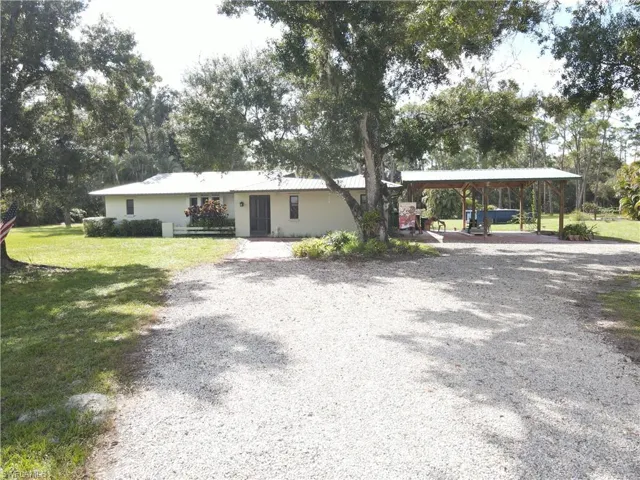 Single story home with a front lawn, gravel driveway, and a carport