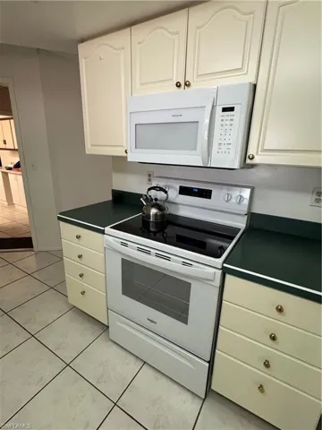 Kitchen with dark green countertops, white appliances, light tile patterned flooring, and white cabinets