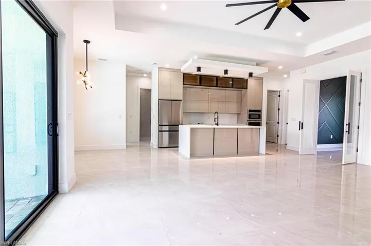 Kitchen featuring modern cabinets, stainless steel refrigerator, a ceiling fan, light countertops, and a center island with sink