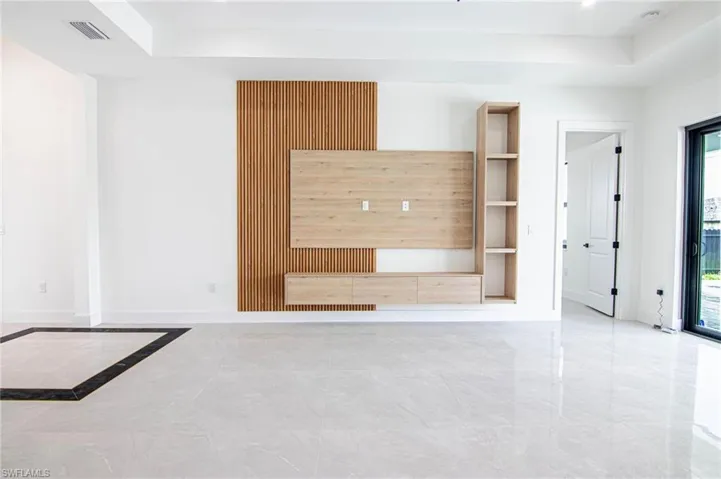 Unfurnished living room featuring a raised ceiling, marble finish flooring, and built in shelves