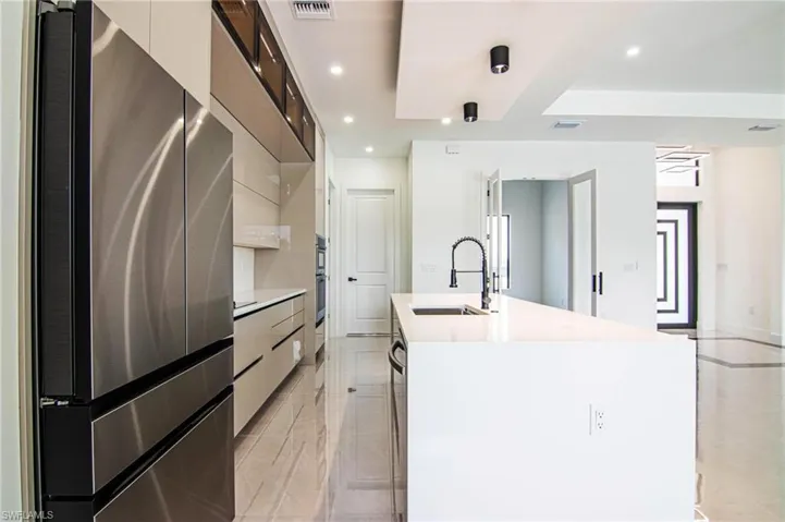 Kitchen with modern cabinets, freestanding refrigerator, light countertops, a center island with sink, and recessed lighting