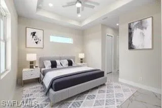 Bedroom with tile floors, ceiling fan, multiple windows, and a raised ceiling