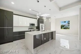 Kitchen featuring a center island with sink, white cabinets, range, and light tile floors