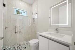 Bathroom with tiled shower, vanity, and toilet