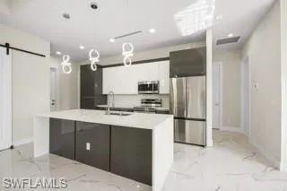 Kitchen with white cabinetry, a center island with sink, stainless steel appliances, a barn door, and sink