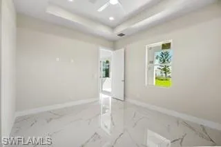 Empty room featuring ceiling fan, a tray ceiling, and tile floors