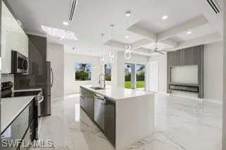 Kitchen featuring an island with sink, light tile flooring, coffered ceiling, sink, and appliances with stainless steel finishes