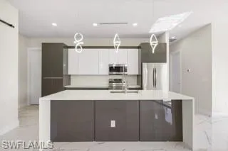 Kitchen featuring stainless steel appliances, an island with sink, white cabinets, sink, and light tile flooring