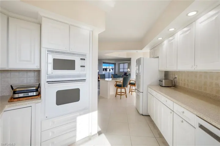 Kitchen with backsplash, white cabinetry, light tile patterned flooring, and white appliances