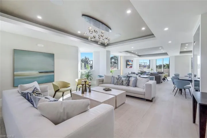 Living room with a raised ceiling, a notable chandelier, and light wood-type flooring