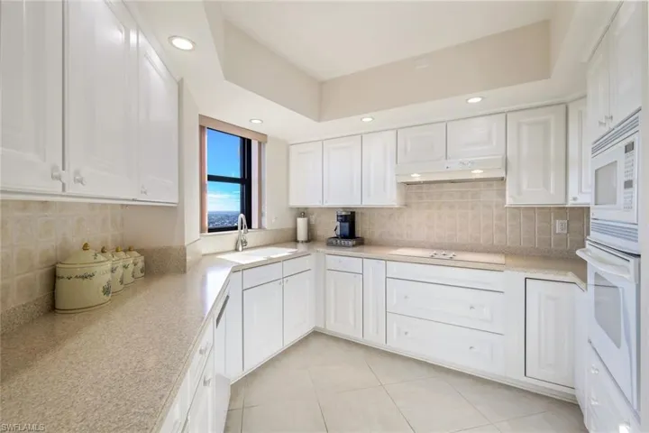 Kitchen with white appliances, sink, decorative backsplash, light tile patterned flooring, and white cabinetry