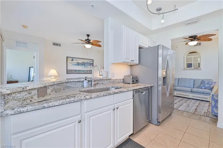 Kitchen featuring ceiling fan, light stone countertops, white cabinets, and appliances with stainless steel finishes