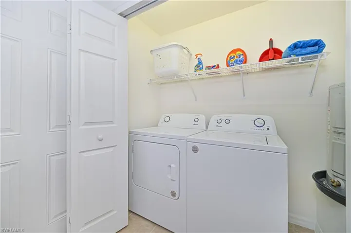 Laundry room featuring washing machine and clothes dryer, light tile patterned floors, and electric water heater