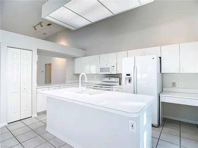 Kitchen with white cabinets, a center island with sink, white appliances, and light tile floors