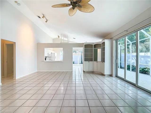 Tiled empty room with track lighting, ceiling fan, and lofted ceiling