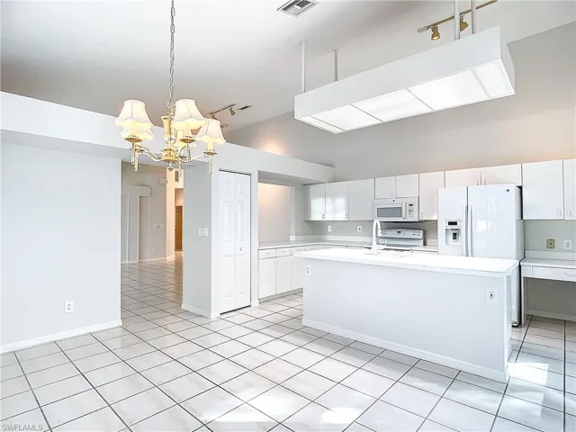Kitchen with white cabinetry, white appliances, decorative light fixtures, track lighting, and light tile floors