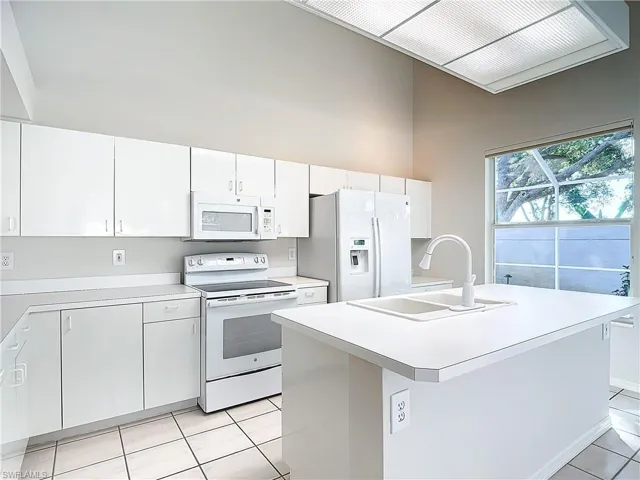 Kitchen with white appliances, light tile floors, sink, a kitchen island with sink, and white cabinetry
