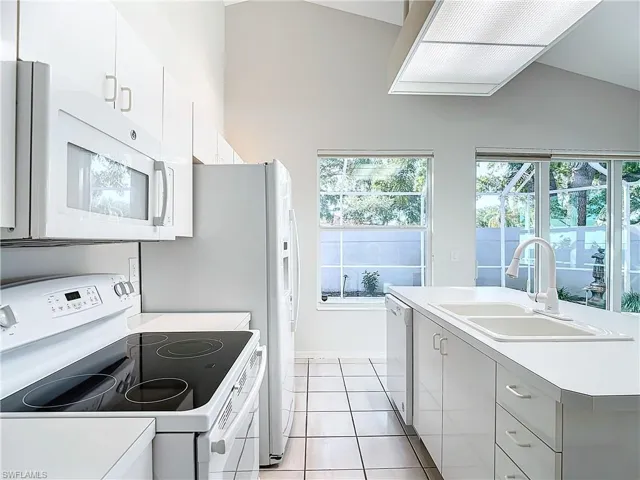 Kitchen with sink, white cabinetry, white appliances, and lofted ceiling