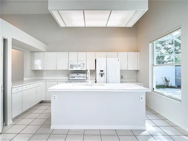 Kitchen featuring a wealth of natural light, an island with sink, and white appliances