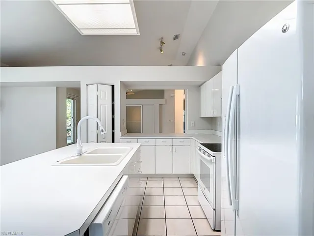 Kitchen featuring light tile flooring, a kitchen island, white cabinets, sink, and white appliances
