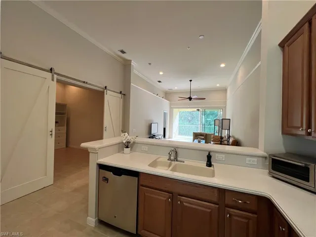 Kitchen featuring kitchen peninsula, ceiling fan, a barn door, ornamental molding, and dishwasher