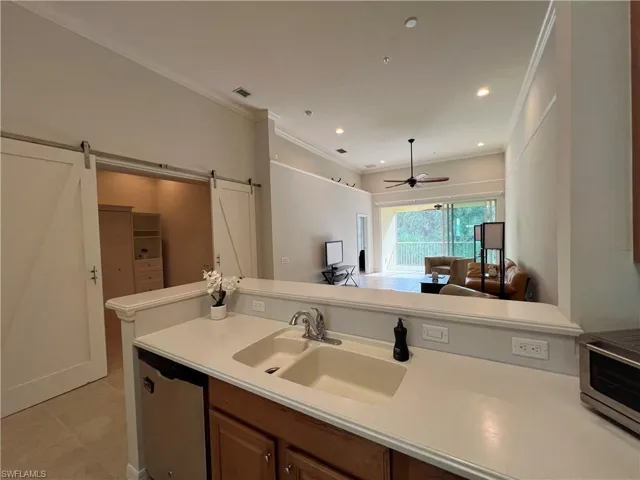 Kitchen featuring dishwasher, ornamental molding, sink, a barn door to the den