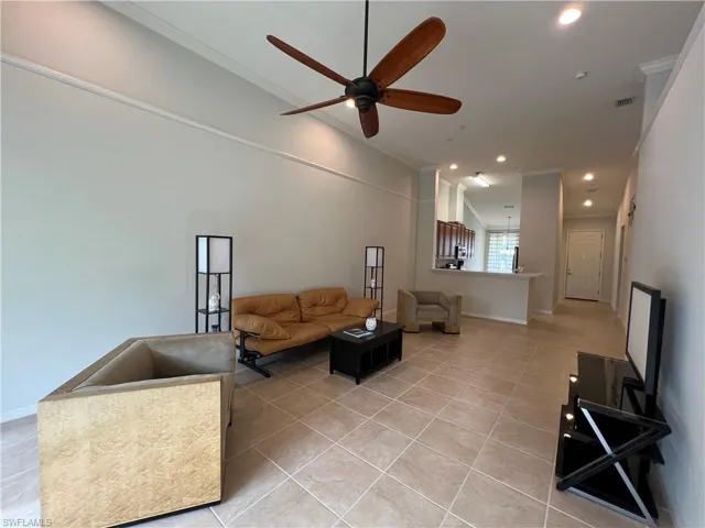 Living room with ceiling fan, ornamental molding, and light tile patterned flooring