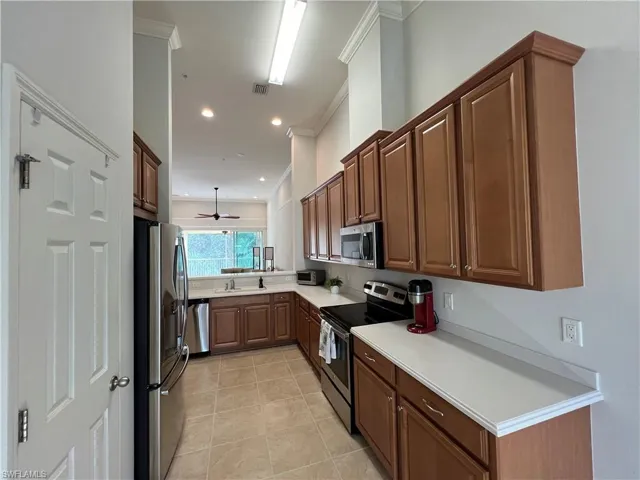 Kitchen with light tile patterned floors, appliances with stainless steel finishes, ceiling fan, crown molding, and sink