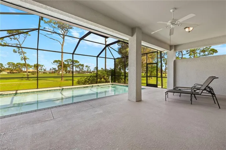 View of swimming pool with ceiling fan, glass enclosure, a patio area, and a lawn