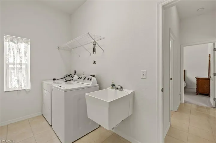 Clothes washing area featuring light tile patterned flooring, sink, and washing machine and clothes dryer