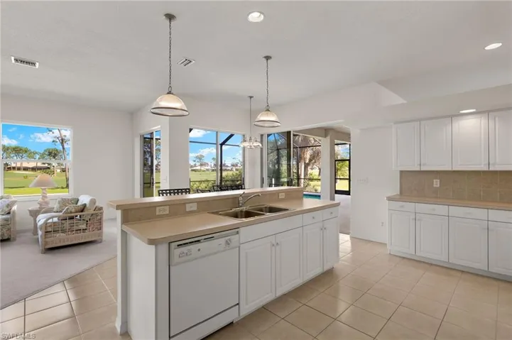 Kitchen featuring sink, dishwasher, an island with sink, hanging light fixtures, and white cabinetry