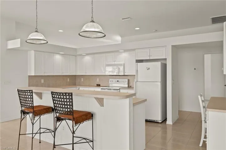 Kitchen featuring white appliances, backsplash, white cabinetry, and light tile patterned floors