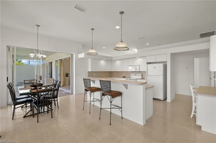 Kitchen with white appliances, a center island, decorative light fixtures, white cabinets, and light tile patterned floors