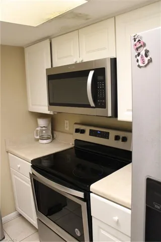 Kitchen with white cabinetry, light tile patterned flooring, stainless steel range oven, and refrigerator