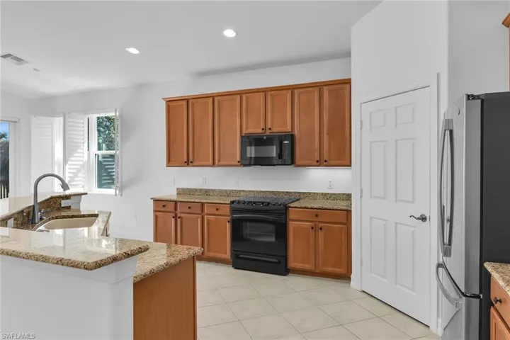 Kitchen featuring black appliances, light stone counters, recessed lighting, light tile patterned flooring, and brown cabinetry
