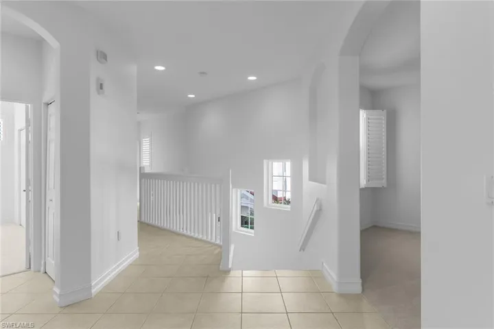 Hall with arched walkways, an upstairs landing, light tile patterned floors, and recessed lighting.