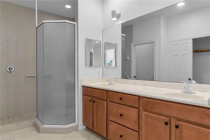 Primary bathroom with a shower stall, double vanity, light tile patterned floors, and recessed lighting.