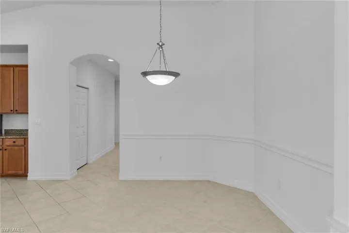 Dining area featuring arched walkways, light tile patterned flooring, and vaulted ceiling.