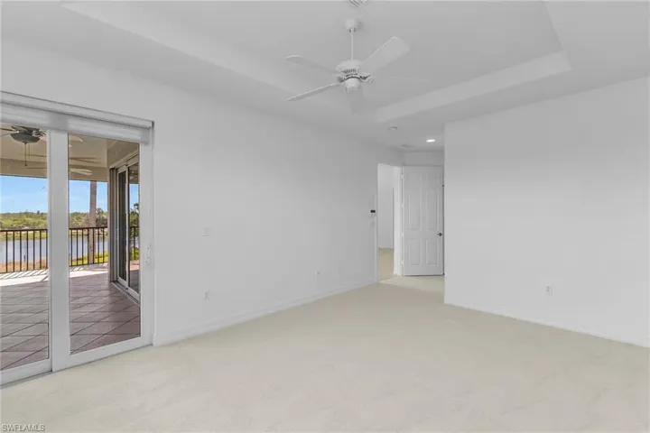Primary bedroom, open to lanai, featuring a raised ceiling, a ceiling fan, light colored carpet, and a water view.