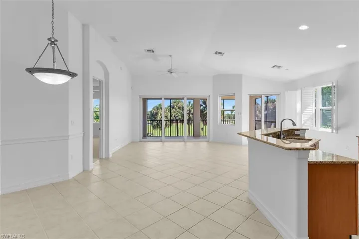 Open great room featuring a kitchen with light stone countertops, a center island with sink, light tile patterned floors, lofted ceiling, pendant lighting, a dining area, and the living room.