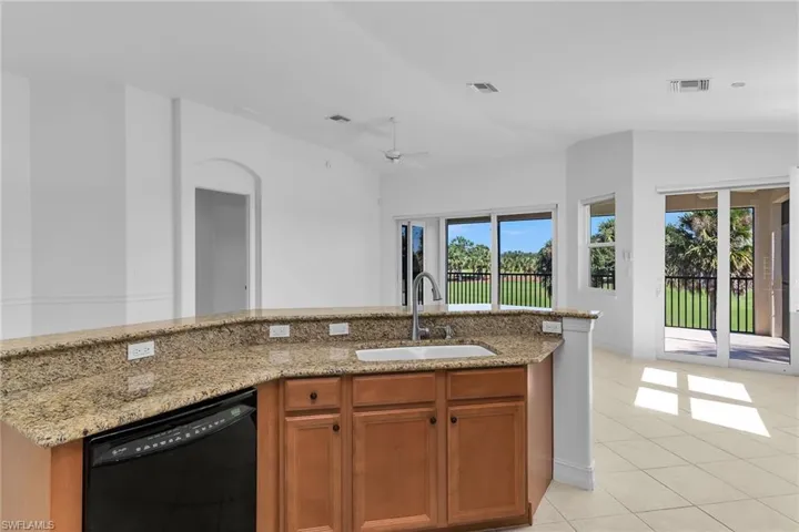 Kitchen with brown cabinets, black dishwasher, light tile patterned floors, light stone counters, and a ceiling fan.