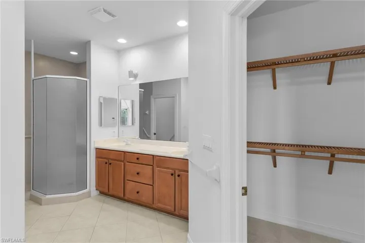Primary bathroom with a spacious closet, double vanity, a stall shower, light tile patterned flooring, and recessed lighting.